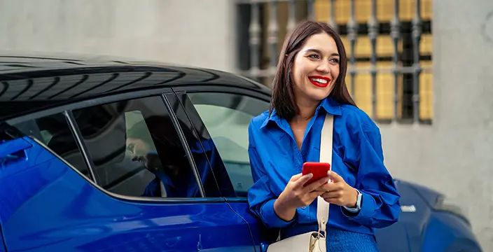 Smiling woman with phone leaning on car